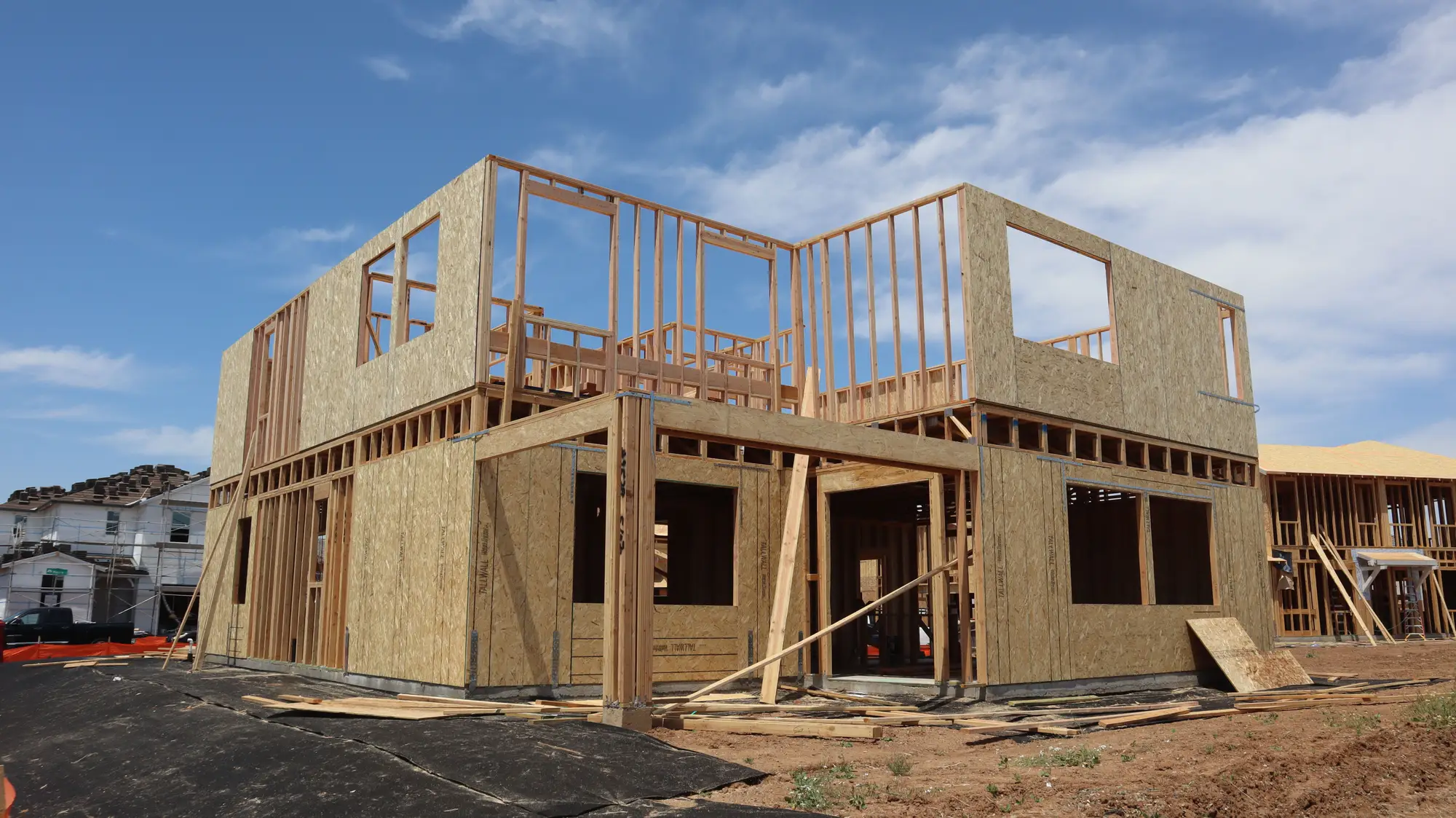 A two-storey timber house frame on a cleared lot, sheathing on part of the walls and the window openings still open