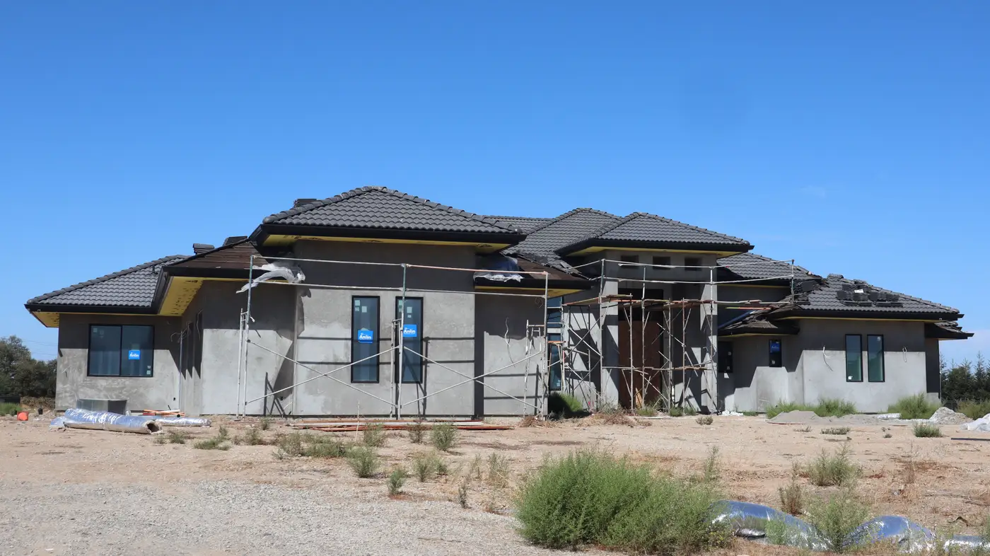 A stucco house nearing completion, with a tiled roof and scaffolding still up around the walls.